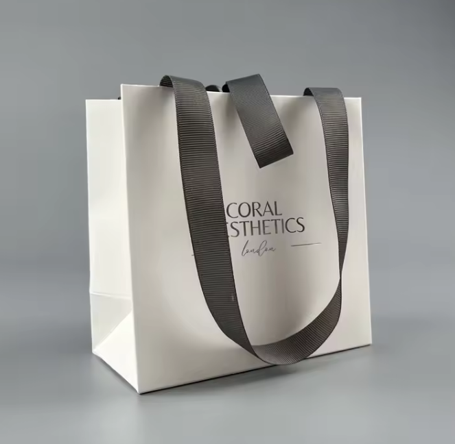 luxury matte white paper gift bag with silver foil logo and gray ribbon bow closure