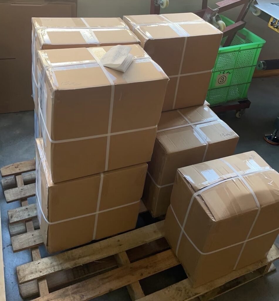 Small‑batch custom packaging orders stacked on wooden pallet, cartons fully packed and strapped, ready for shipment from factory warehouse